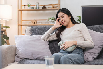 Obraz premium Young Woman Experiencing Abdominal Pain and Headache During Menstruation While Sitting on a Sofa at Home