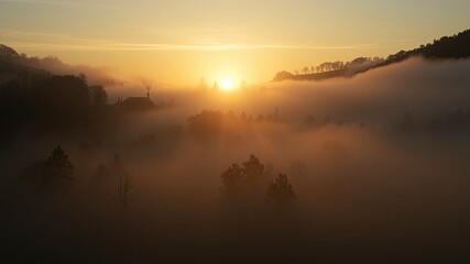 Fototapeta premium Golden Sunlight Filters Through Mist Enveloping a Hillside Village with a Smoke Plume Rising From a Distant Chimney