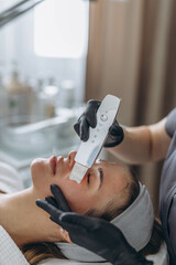 Cosmetologist making facial treatment with ultrasonic spatula to young woman.