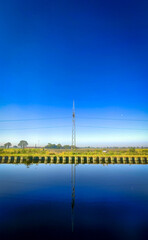 A serene view showcasing a peaceful reflection in still water under a clear blue sky with distant landscape