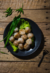 Pork-filled sago in a black plate with long leaf coriander and lettuce on an old wooden table with green chilli peppers on a wooden table