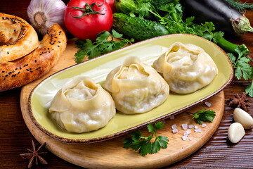 Appetizing manti with meat in a plate against the background of fresh vegetables, on a wooden board. Restaurant, cafe, lunch, close-up.