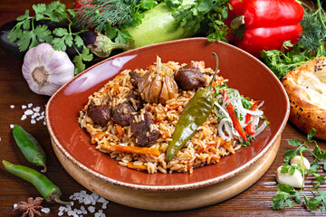 Traditional Uzbek pilaf with meat on a wooden board with fresh vegetables in the background. Cafe, lunch, close-up.