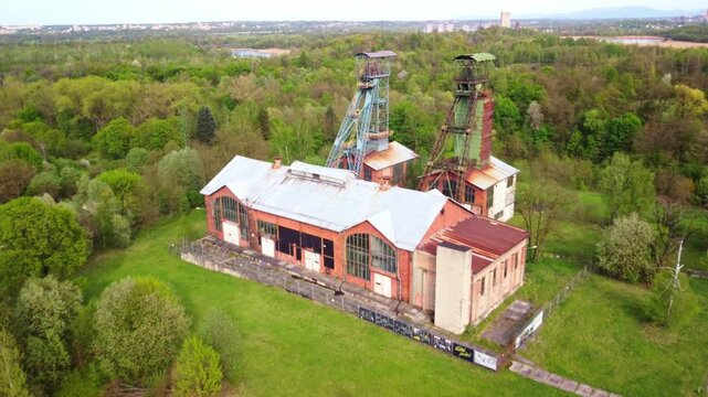 Aerial drone dolly to old coal mine surrounded by autumn trees and overgrown landscape, Czech Republic, rusted tower and chutes