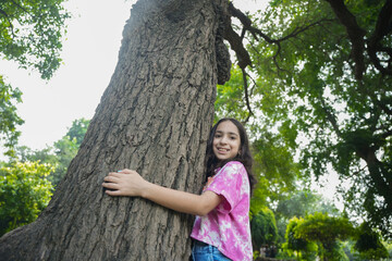 cute young indian girl child embracing large tree. Save planet, ecology, climate change, nature...