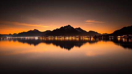 Obraz premium serene landscape featuring mountains reflecting in calm lake at sunset, with warm orange hues illuminating sky and water. tranquil scene evokes sense of peace and natural beauty