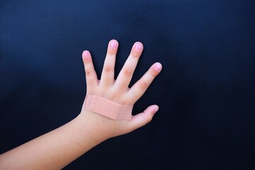 A toddler puts his hand on a dark background where the top of his hand is wrapped in plaster because he has a wound. With a close look.