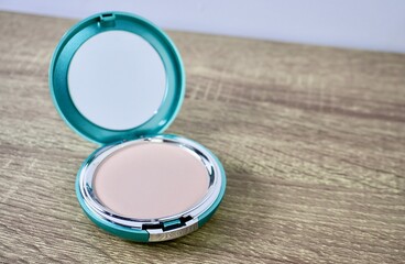 Compact powder light shade make up in round box container isolated on horizontal ratio brown wooden table surface background.