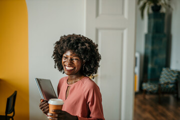 A modern black woman with a coffee cup smiles confidently in an office environment, embodying...