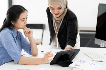 Fototapeta premium Happy female entrepreneurs using a tablet as they brainstorm ideas for their business. Two business women working as a team to achieve success
