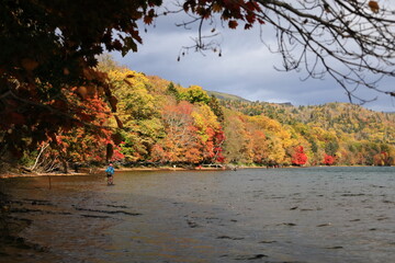 紅葉の湖畔で釣りをする人