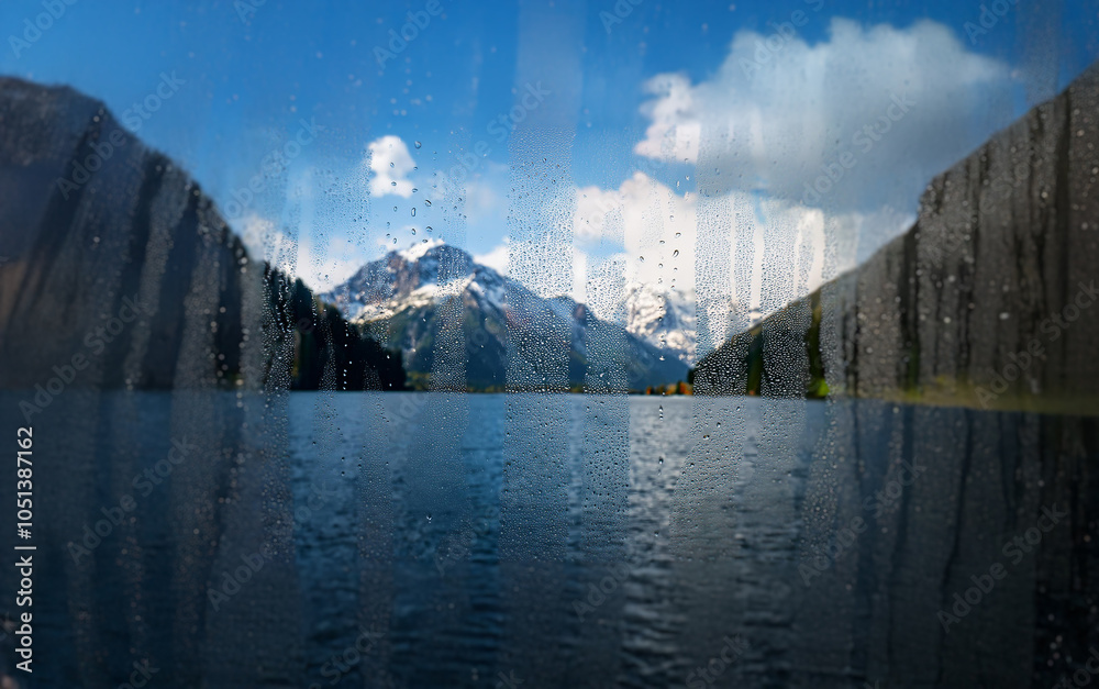 Poster A view of a lake and snow-capped mountains through a rain-streaked window.