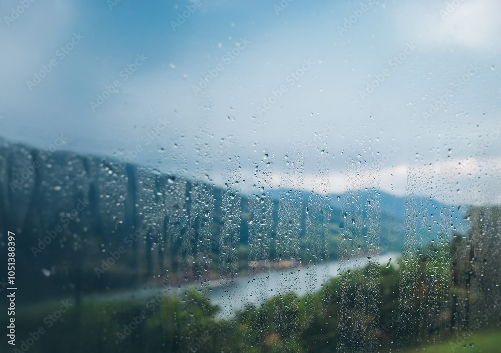Poster Raindrops on a windowpane obscure a view of a river, trees, and mountains.