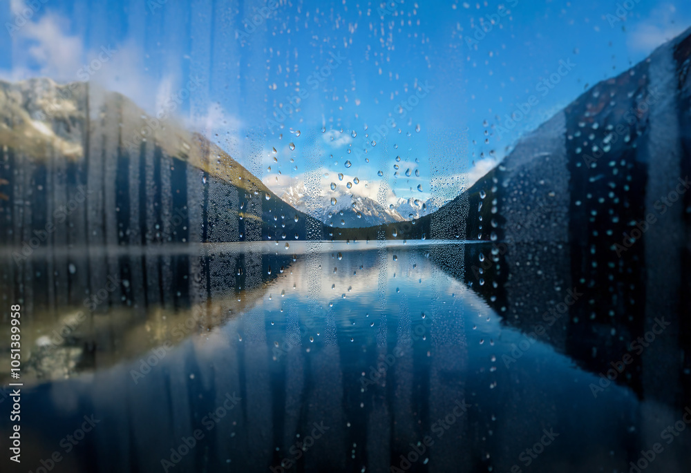 Poster A view of a mountain range reflected in a still lake through a window covered in raindrops.