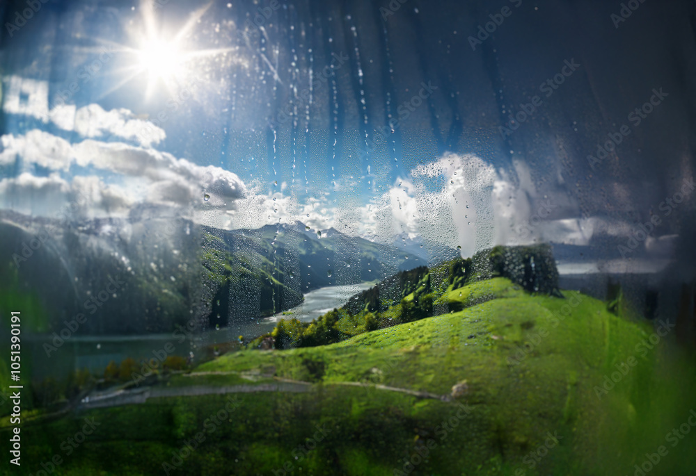 Poster a view of a mountain range and a river, seen through a window with raindrops. the sun shines brightl