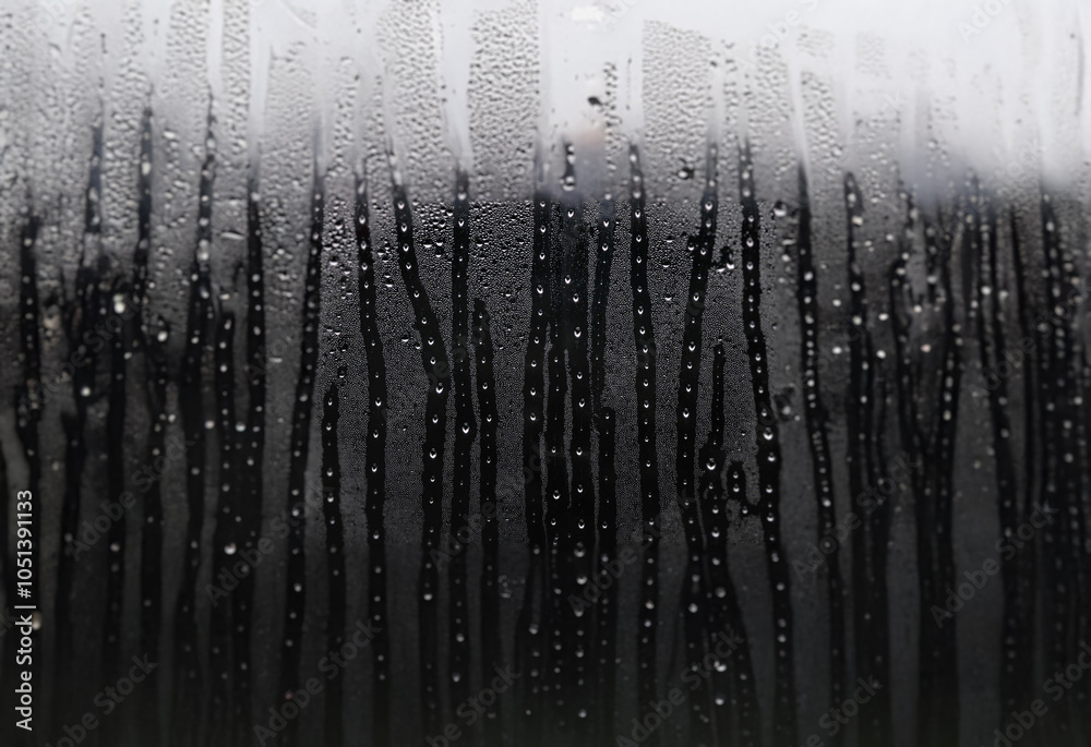 Fototapete a close-up view of condensation on a windowpane. the droplets form streaks and patterns against a bl
