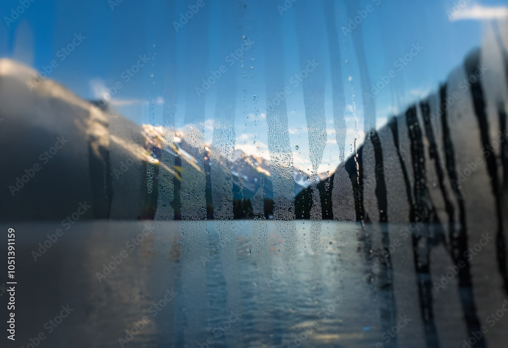 Poster A blurry view of a snow-capped mountain range through a rain-streaked window.