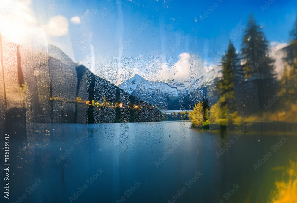 Poster A view of a mountain lake through a wet windowpane.  The sun is setting, casting a warm glow on the scene.  The water is calm, and the mountains are reflected in the surface.