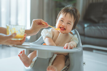 Closeup of Happy asian baby girl eating first food pumpkin from spoon with mom at home