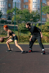 Fototapeta premium close up a sports ground basketball field active recreation girl with short hair in shorts and yellow T-shirt with black-haired guy playing basketball hitting the hoop