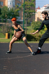 Fototapeta premium close up a sports ground basketball field active recreation girl with short hair in shorts and yellow T-shirt with black-haired guy playing basketball hitting the hoop