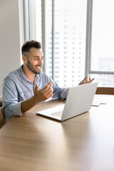 Fototapeta premium Cheerful positive Latin entrepreneur man talking on video call at laptop, discussing Internet project on online conference chat, speaking at computer, moving hands, smiling, laughing