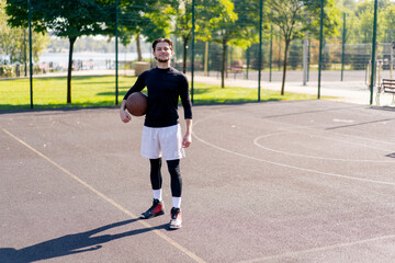 Obraz premium a sports ground basketball field active recreation guy in white shorts and black t-shirt stands with ball in hands posing in front of camera