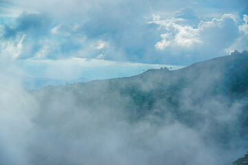 Obraz premium A serene landscape with hills shrouded in mist under a cloudy sky.