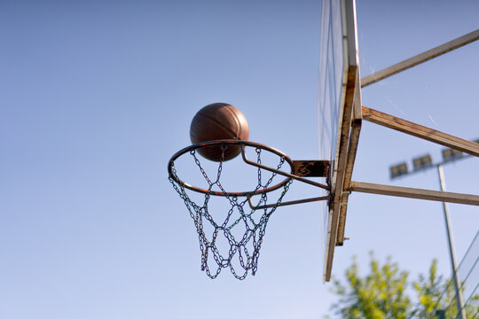 a sports ground basketball field shot from below basketball hoop with chains hitting the target basketball against the sky