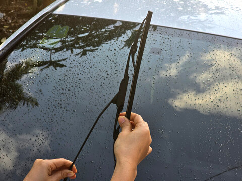 The driver's hand holds the wet windshield wiper, replacing the worn wiper rubber to avoid scratches on the car's windshield.