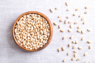 Pine nuts in a wooden bowl on linen fabric. Also known as pinon, pinoli, or pignoli. Shelled seeds...