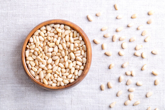 Pine nuts in a wooden bowl on linen fabric. Also known as pinon, pinoli, or pignoli. Shelled seeds and fruits of Korean pines, Pinus koraiensis. Used for pesto, added to dishes or baked into bread.