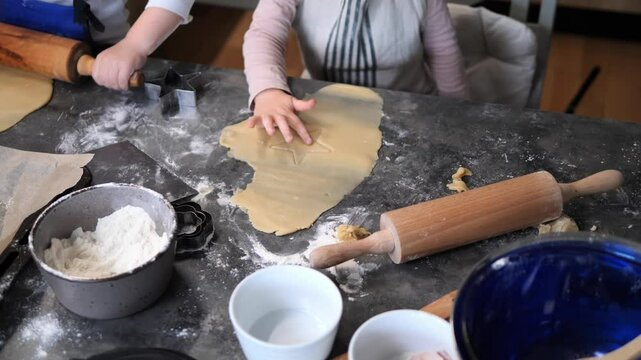 Happy little children work to make dough, aprons dusted with flour. Boys and girls press and roll dough with eager hands, learning and enjoying the simple art of crafting from scratch.