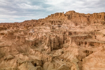 A breathtaking aerial view of a rugged desert canyon landscape at golden hour, showcasing dramatic rock formations, sandy terrain, and a winding road under a clear sky