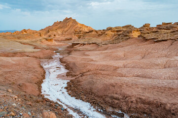 A breathtaking aerial view of a rugged desert canyon landscape at golden hour, showcasing dramatic rock formations, sandy terrain, and a winding road under a clear sky