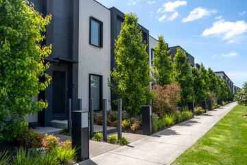 Sleek urban row of modern townhouses with contemporary landscaping and tree-lined pedestrian walkways. Residential street view in an Australian suburban neighborhood featuring small front yards.