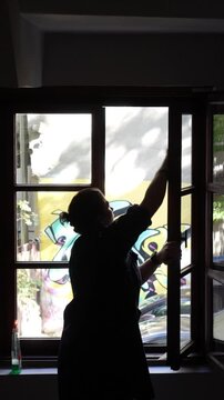 A middle-aged housemaid cleaning dirty window in the stairwell of the hotel by using cloth and detergent. Female housekeeper working indoors. Commercial cleaning company on hotel business concept