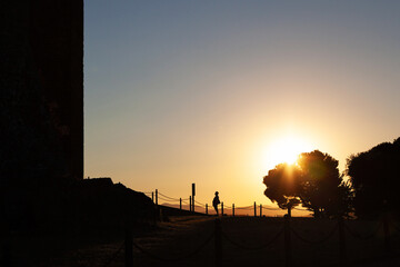 A tourist reading a sign in front of the castle entrance against the backdrop of the setting sun.