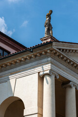 This grand villa showcases Palladian architecture with a stately colonnade, sculpted statues on the roofline, and arched entrances. A serene garden and central well enhance the classical ambiance.
