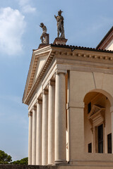 This grand villa showcases Palladian architecture with a stately colonnade, sculpted statues on the roofline, and arched entrances. A serene garden and central well enhance the classical ambiance.