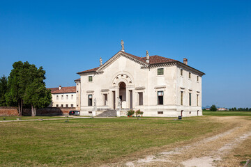 This grand villa showcases Palladian architecture with a stately colonnade, sculpted statues on the roofline, and arched entrances. A serene garden and central well enhance the classical ambiance.