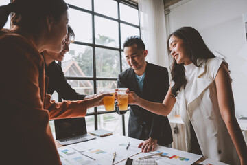 Team of business men and women sitting at desks with documents, graphs, charts, holding glasses of champagne, clinking beers, celebrating a party in business success together in the office.