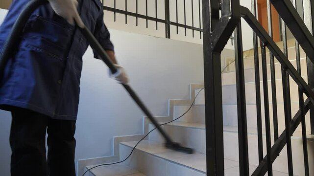 Middle-aged male cleaning up in the stairwell of the hotel with a vacuum cleaner. Commercial cleaning company on hotel business concept