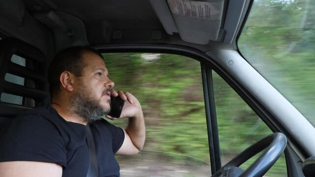 A truck driver dangerously talks on the phone while driving, highlighting risky behavior and lack of attention to the road, posing a threat to road safety.