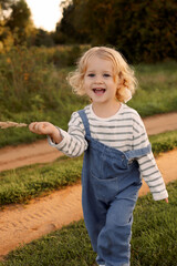 A young blonde girl in a blue jumpsuit walks along a dirt road in the park. High quality photo