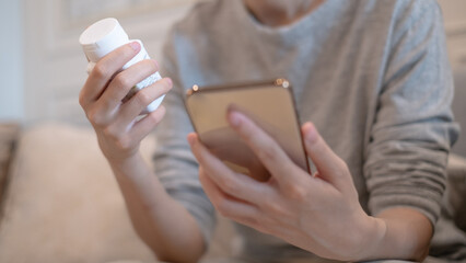 Adults holding vitamin medicine using smartphone mobile phone searching reading looking drug pharmacy nutritional supplement label prescription instructions for rational drug use illness prevention