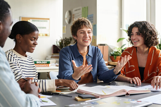 Teacher interacting with diverse group of engaged students during study session around table, with books and educational materials in background, creating a collaborative learning atmosphere