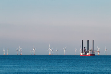 Jack up wind turbines installation vessel in the sea, with wind farm on the background.
