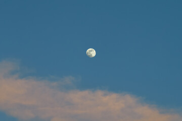 Full moon in the blue sky, with clouds, on a bright day.
