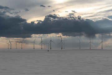 Offshore wind turbines farm in the ocean with dramatic sky and calm water. 